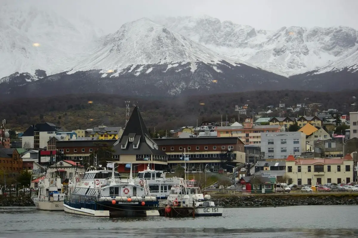 A scenic view of Ushuaia port in Argentina with boats and snow-capped mountains in the background.