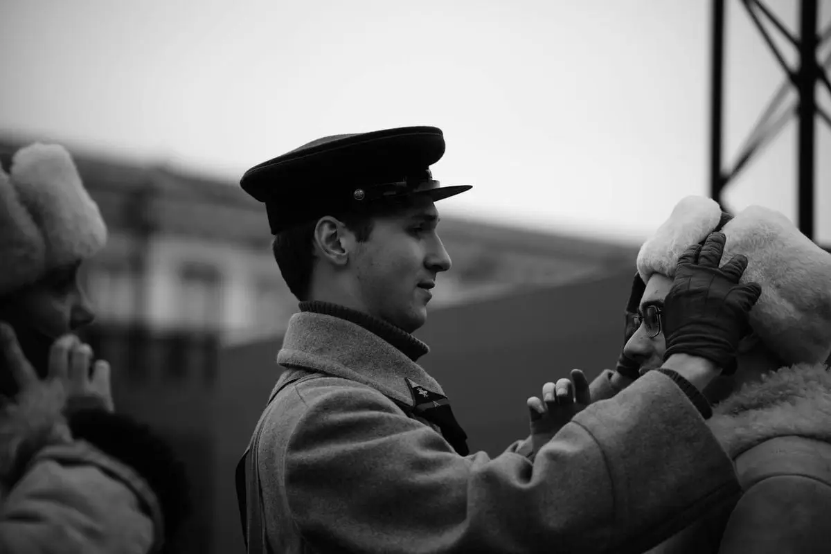 Soldier adjusts hat for friend in cold outdoor setting.