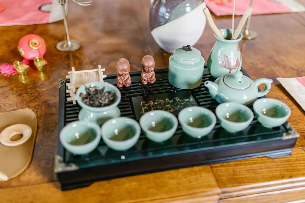 Intricately designed Asian ceramic tea set with teacups, teapot, and tray on a wooden table.