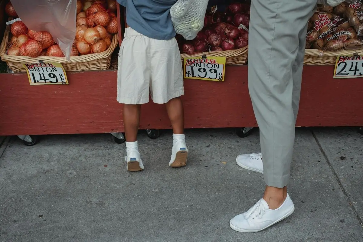 A child and adult picking fresh onions at a local farmers market outdoor stand.