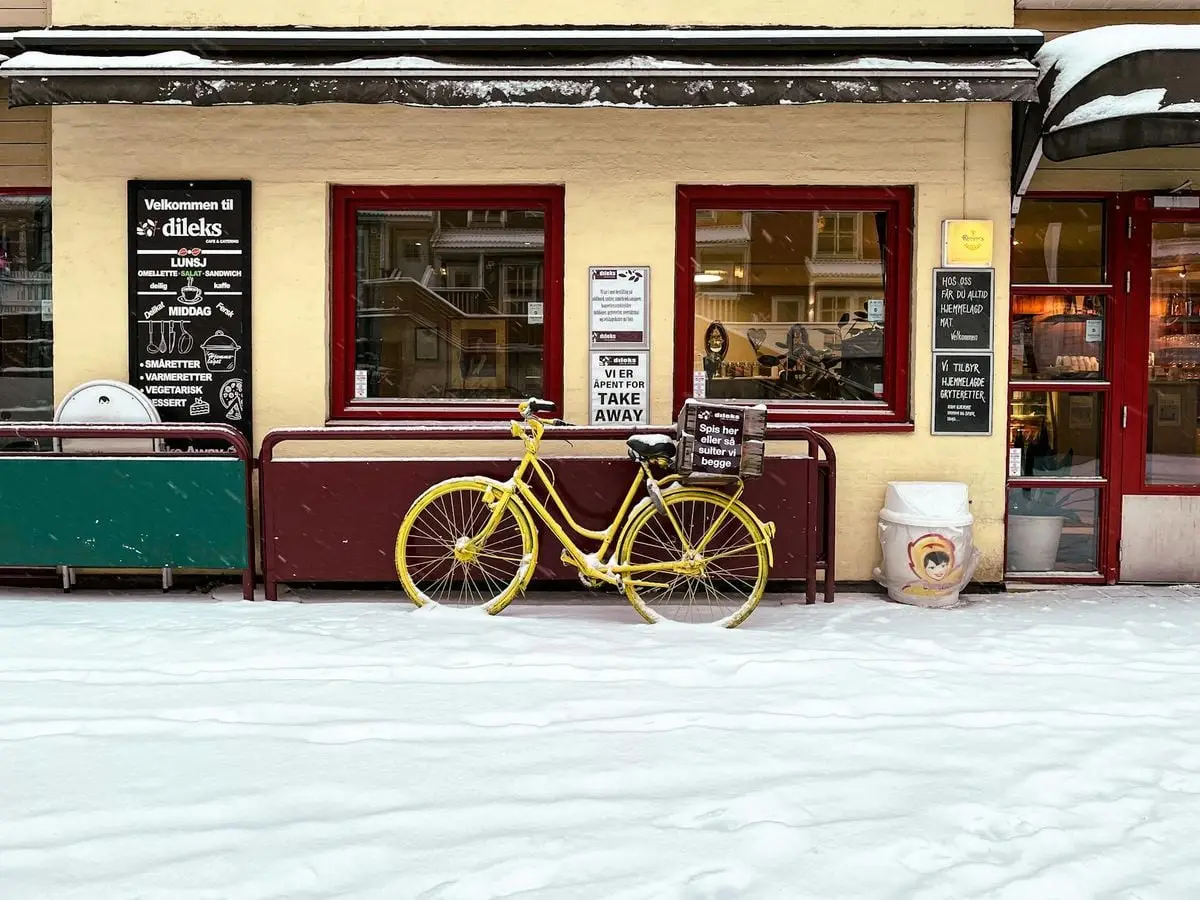 A vibrant yellow bike parked outside a Scandinavian cafe on a snowy winter street.