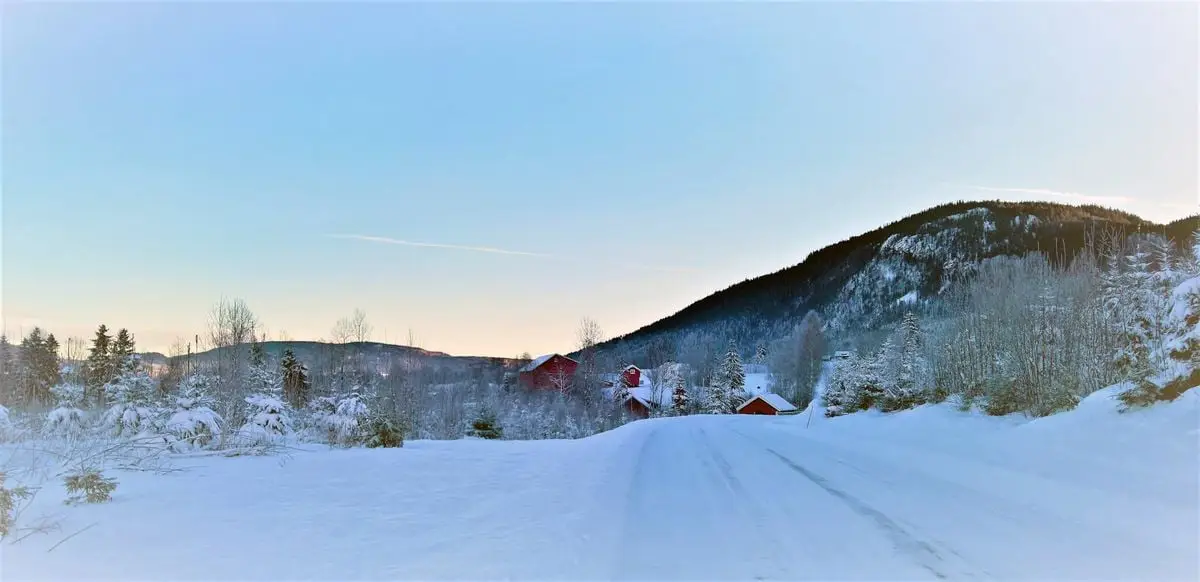 Scenic winter landscape in Hol, Norway with snow-covered mountains and trees under a clear blue sky.