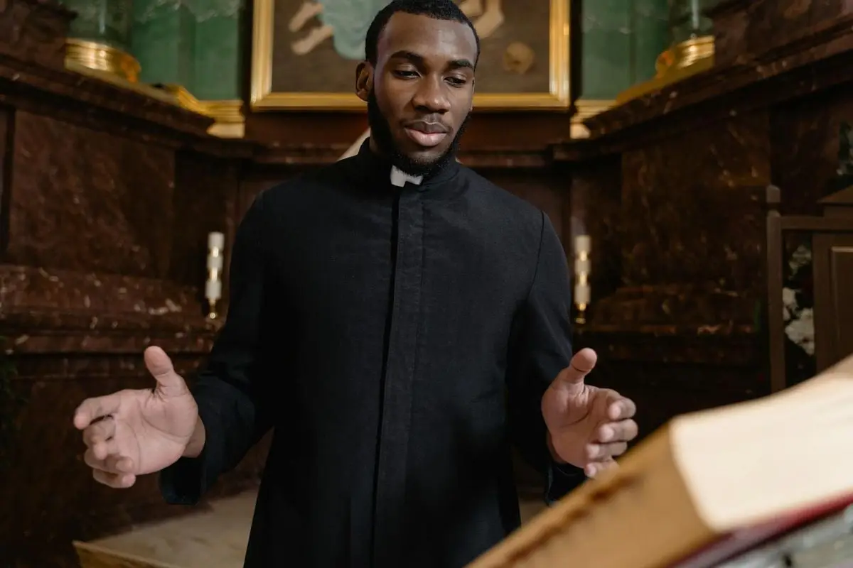 Priest in black vestment conducting a ceremony at a church altar with open book.
