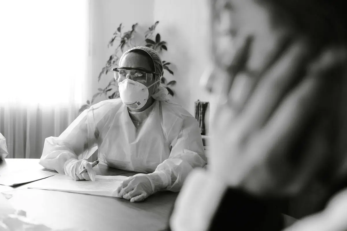 Medical professional in PPE conducting a consultation in a clinical setting.