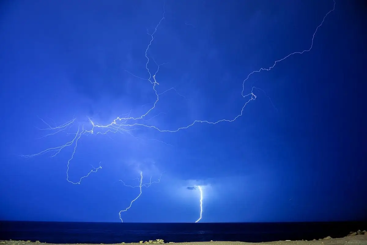A stunning display of lightning bolts illuminating the night sky over a calm sea.