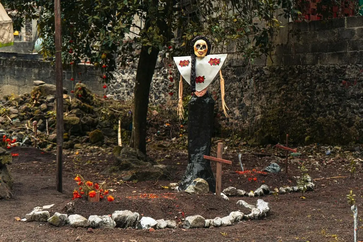 An artistic Catrina statue stands amidst graves, symbolizing Mexican heritage and Halloween.