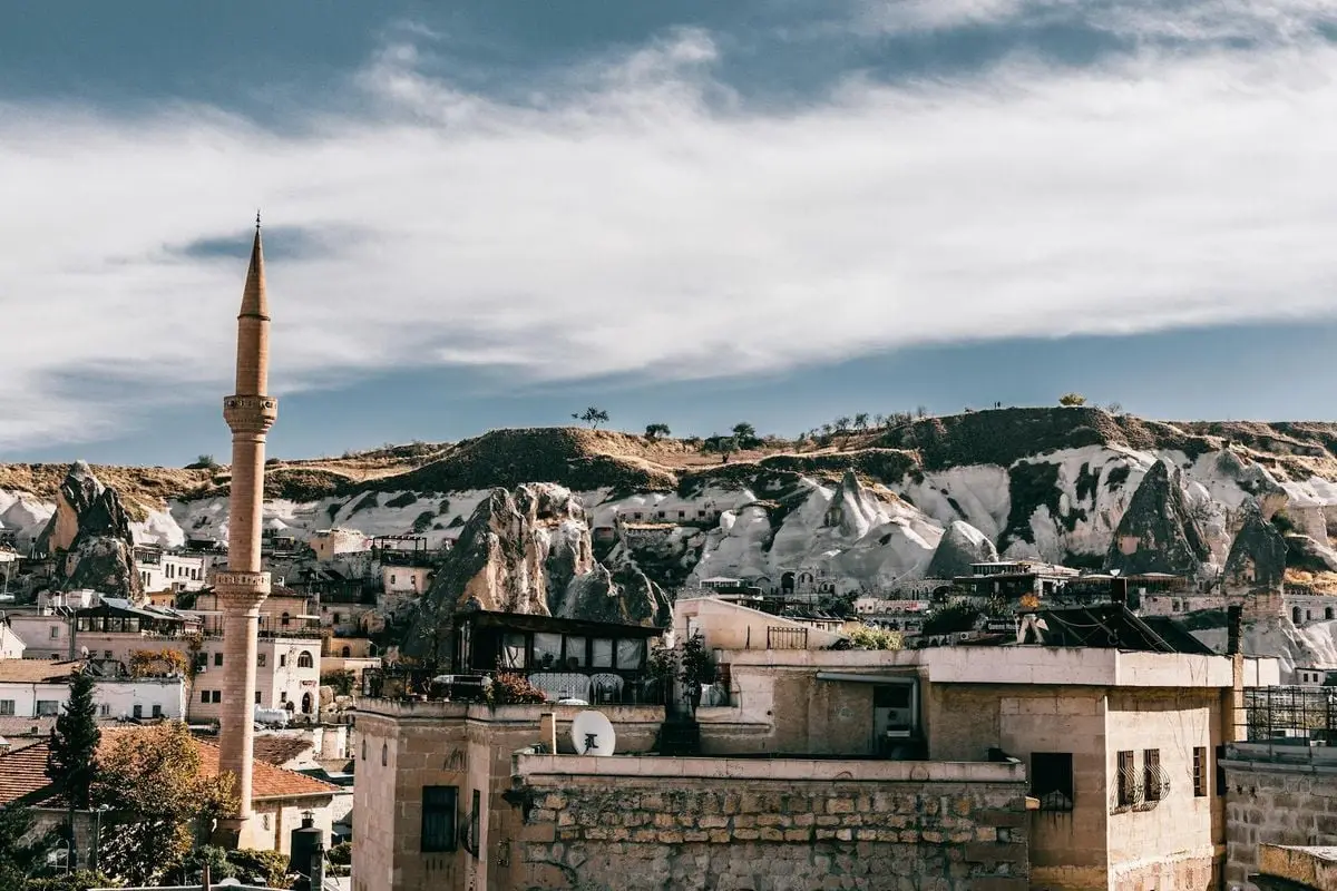 Tall tower located near old houses amidst hilly terrain in ancient town Cappadocia in national park Goreme against cloudy sky