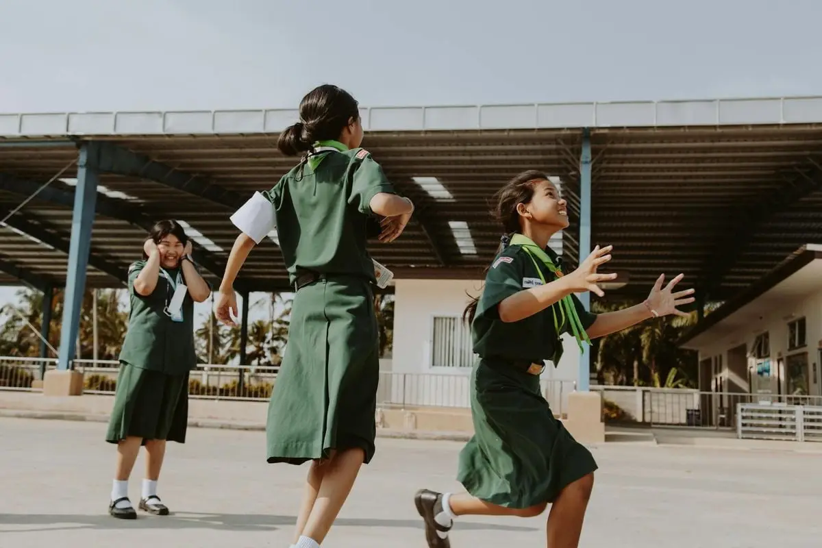 Three girls joyfully playing outside wearing school uniforms, expressing youthful energy.