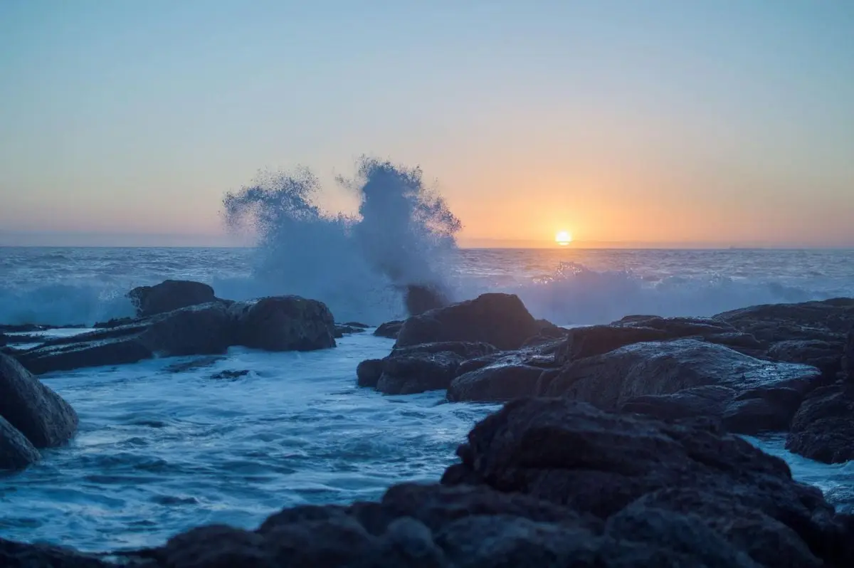 Vivid sunset over ocean waves crashing on rocky shore in Cape Town's scenic coastline.