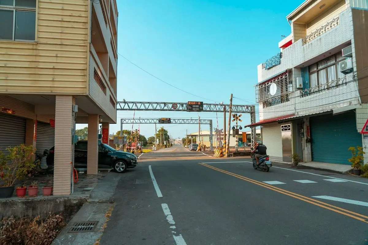 A peaceful urban street with buildings and a motor scooter passing by.