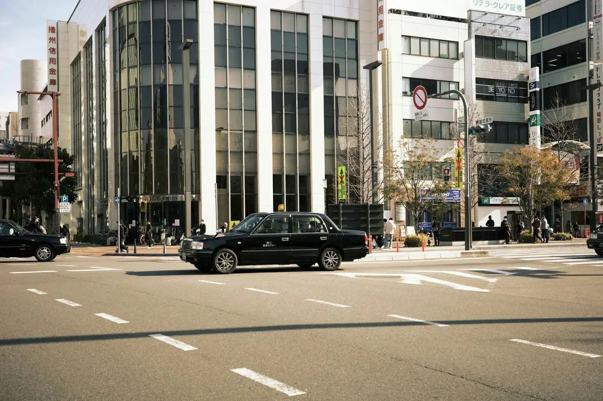Busy city intersection with taxis and modern buildings on a sunny day.