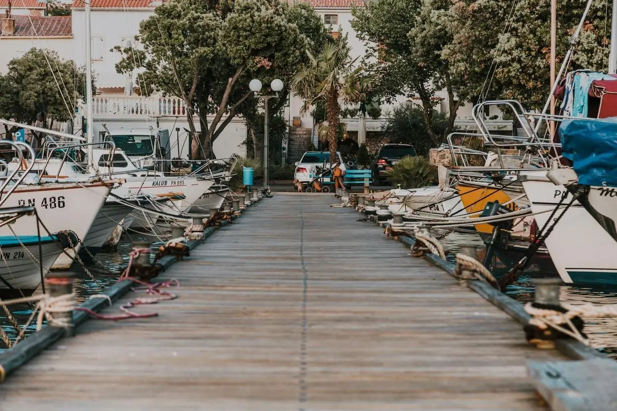 A serene marina with sailboats and yachts docked along a wooden pier in a picturesque coastal town.