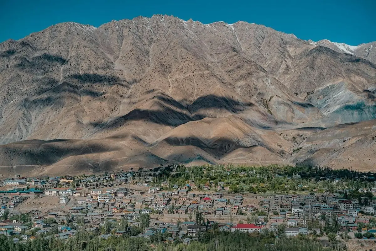 Stunning aerial view of Leh town nestled against rugged mountain backdrop in clear blue skies.