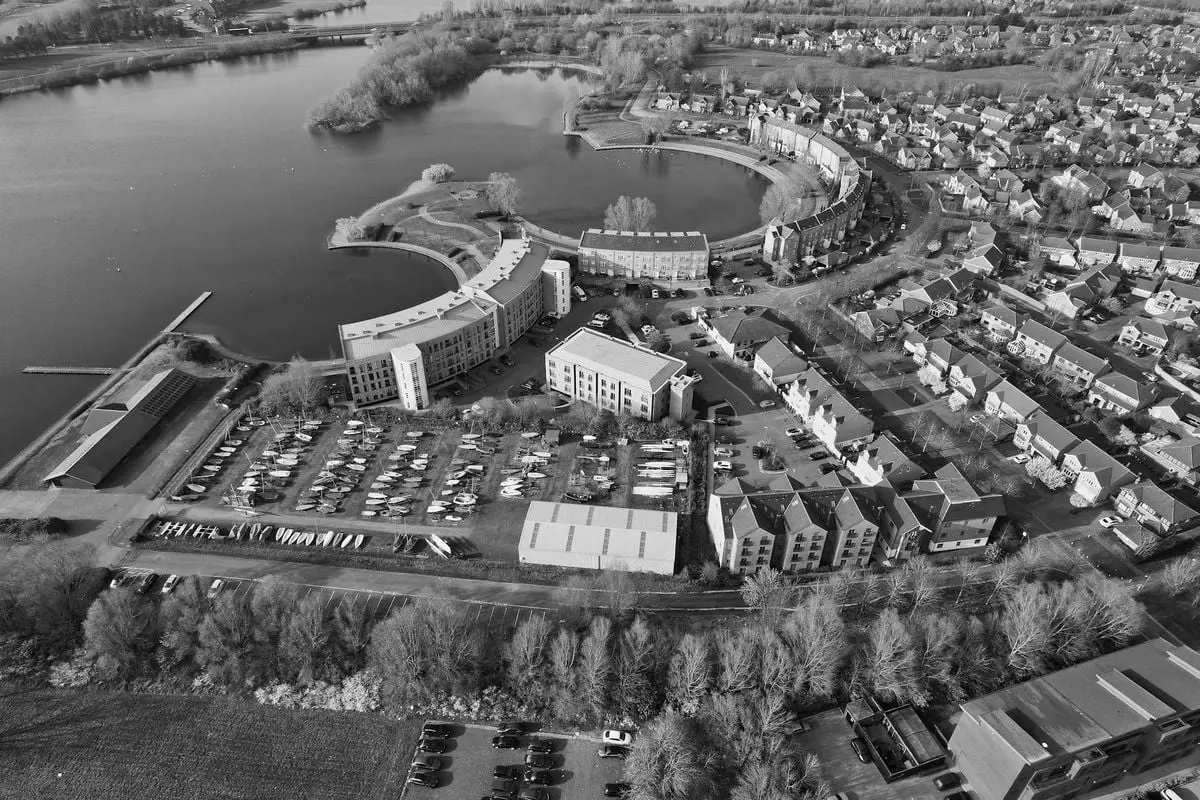 Black and white aerial view of Caldecotte Lake and surrounding urban area in England.