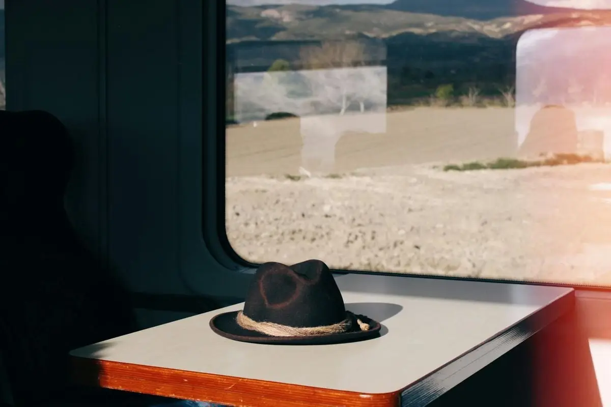 A stylish hat rests on a train table, capturing a serene journey through the countryside.
