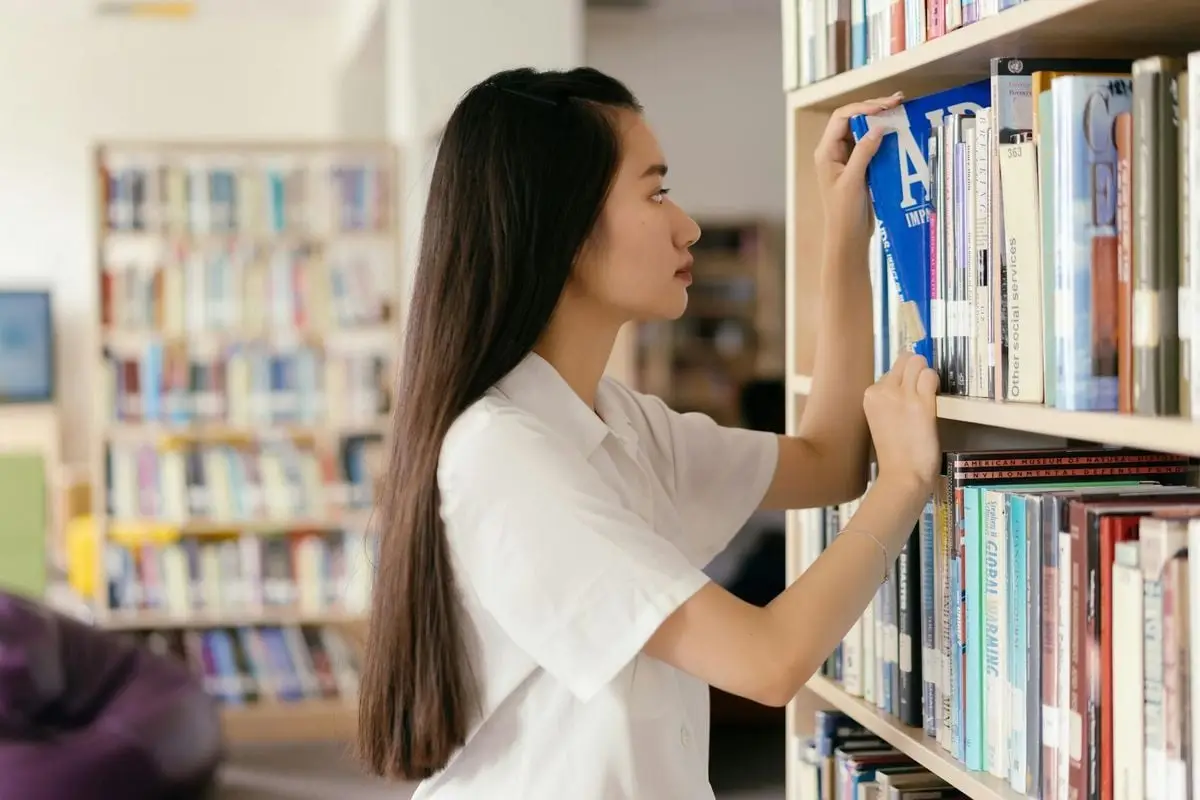 Asian woman browsing books in a library, focused on learning and research.