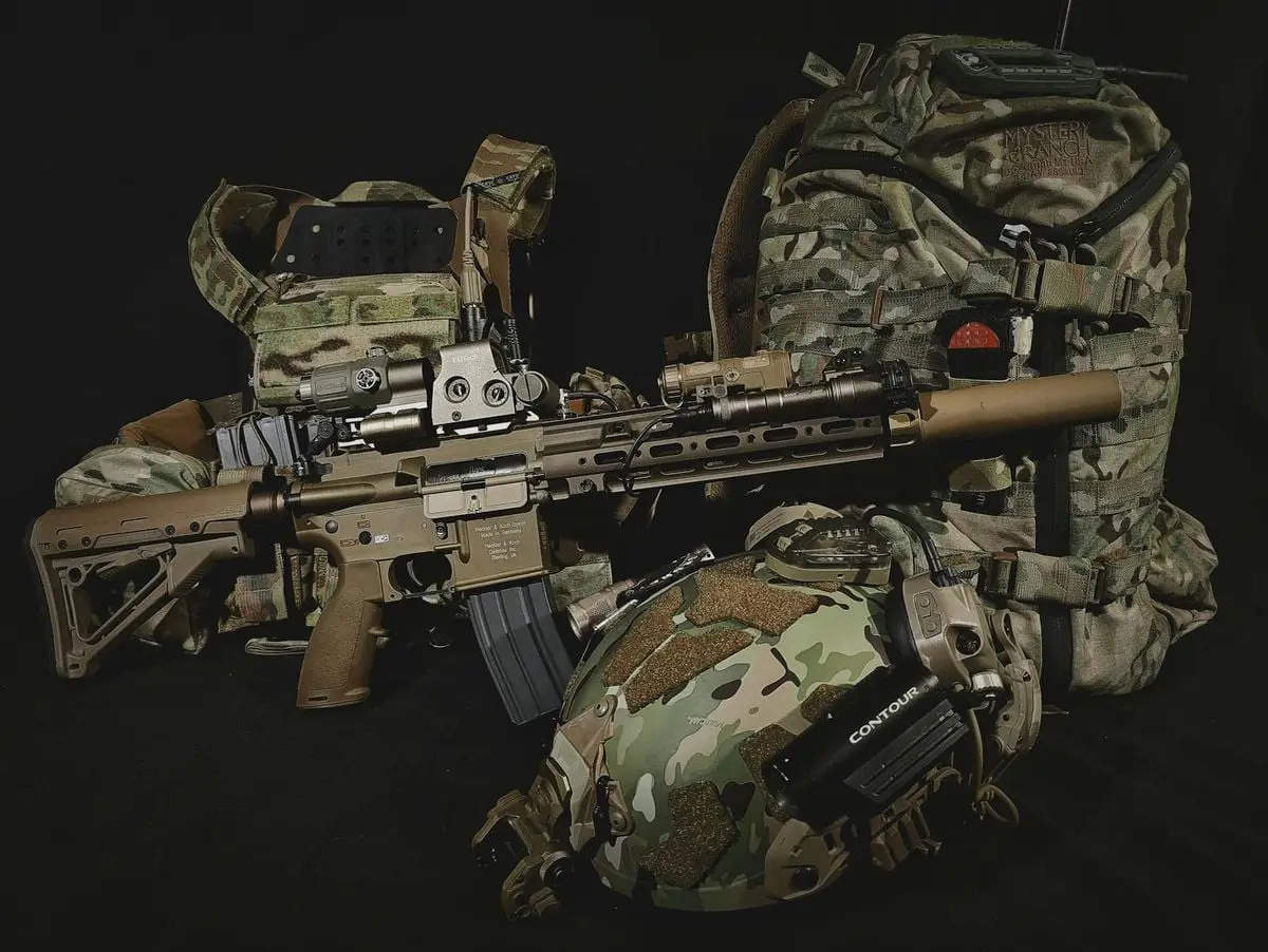 Close-up of tactical military gear including rifle, backpack, and helmet in camouflage.