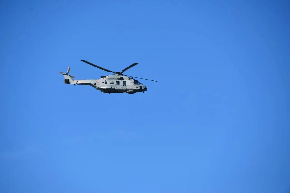 A military helicopter flies against a clear blue sky, showcasing advanced aviation technology.