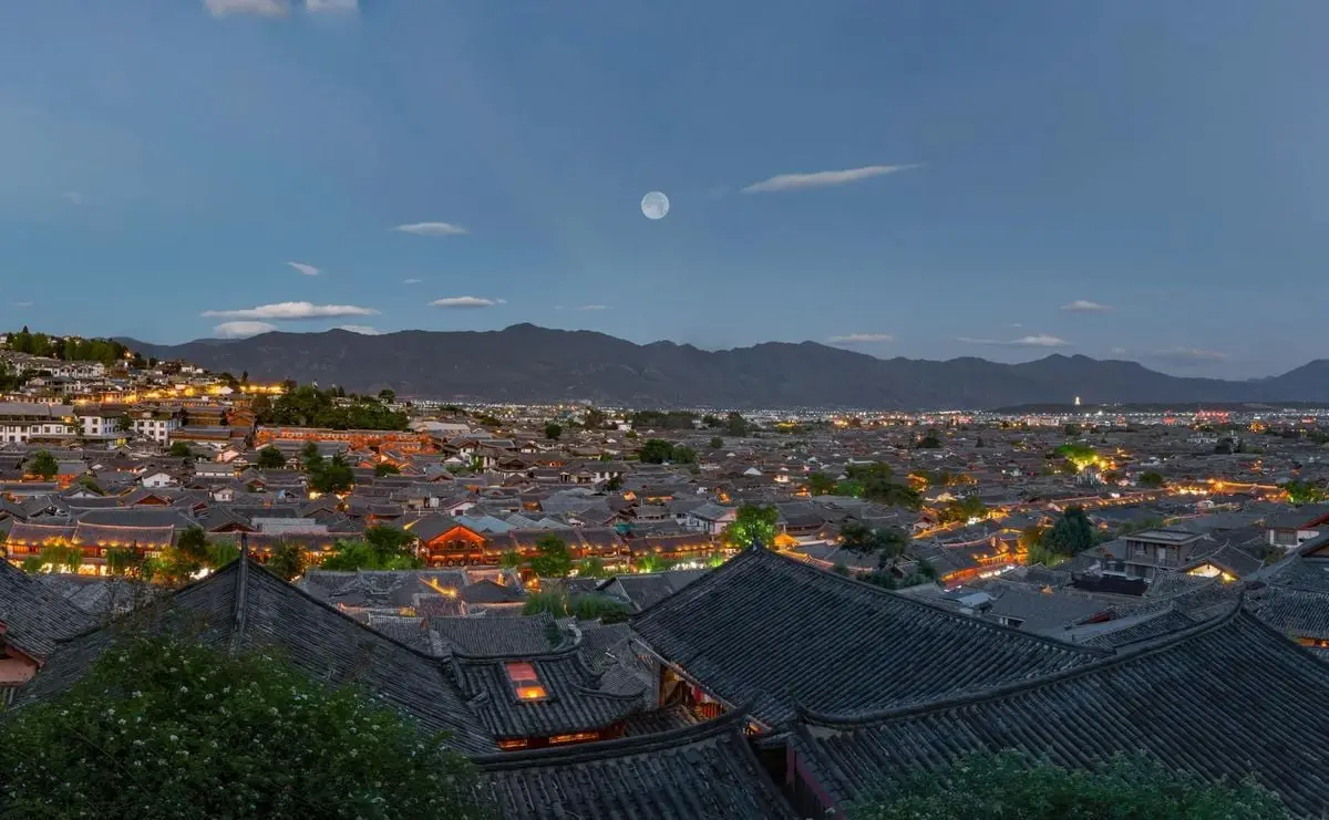 Discover the mesmerizing twilight view of Lijiang Ancient Town with traditional rooftops and mountains.