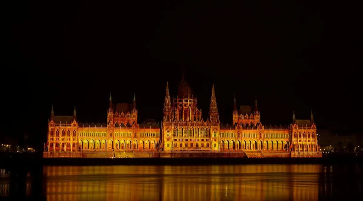 Illuminated Budapest Parliament reflecting on the Danube River at night.