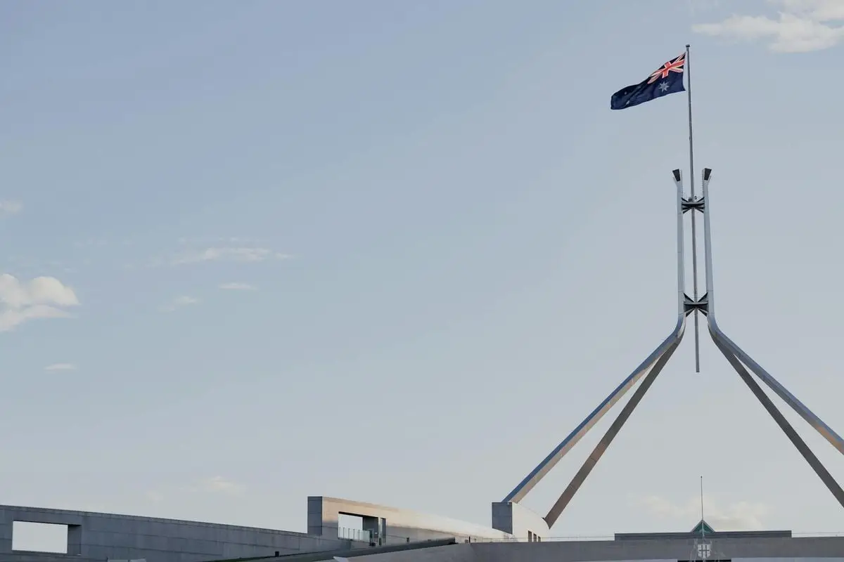Canberra's iconic Australian Parliament House with national flag against a clear blue sky.