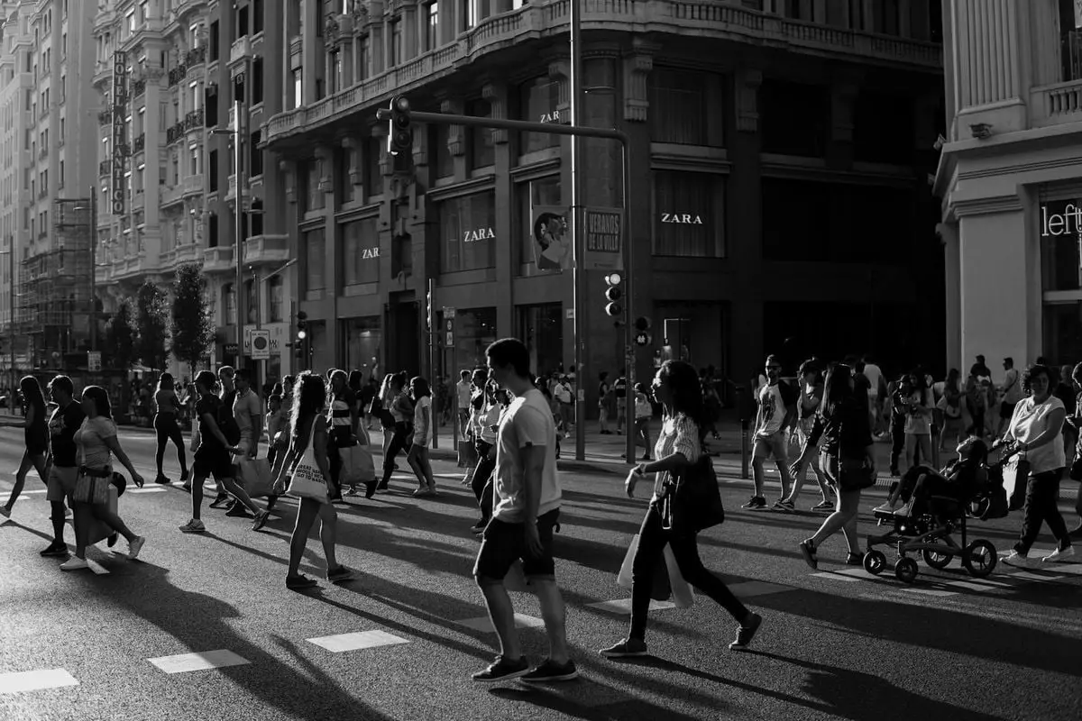 Black and white photo of people crossing a busy street in Madrid, Spain.