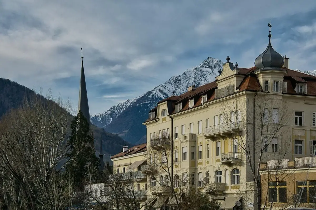 Beautiful architecture in Meran, Italy, set against snow-capped mountains.