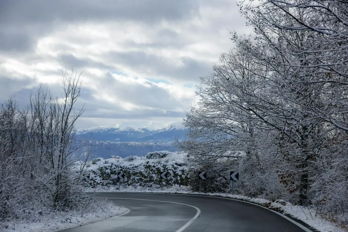 A picturesque snowy road winding through a winter landscape with mountains in the background.