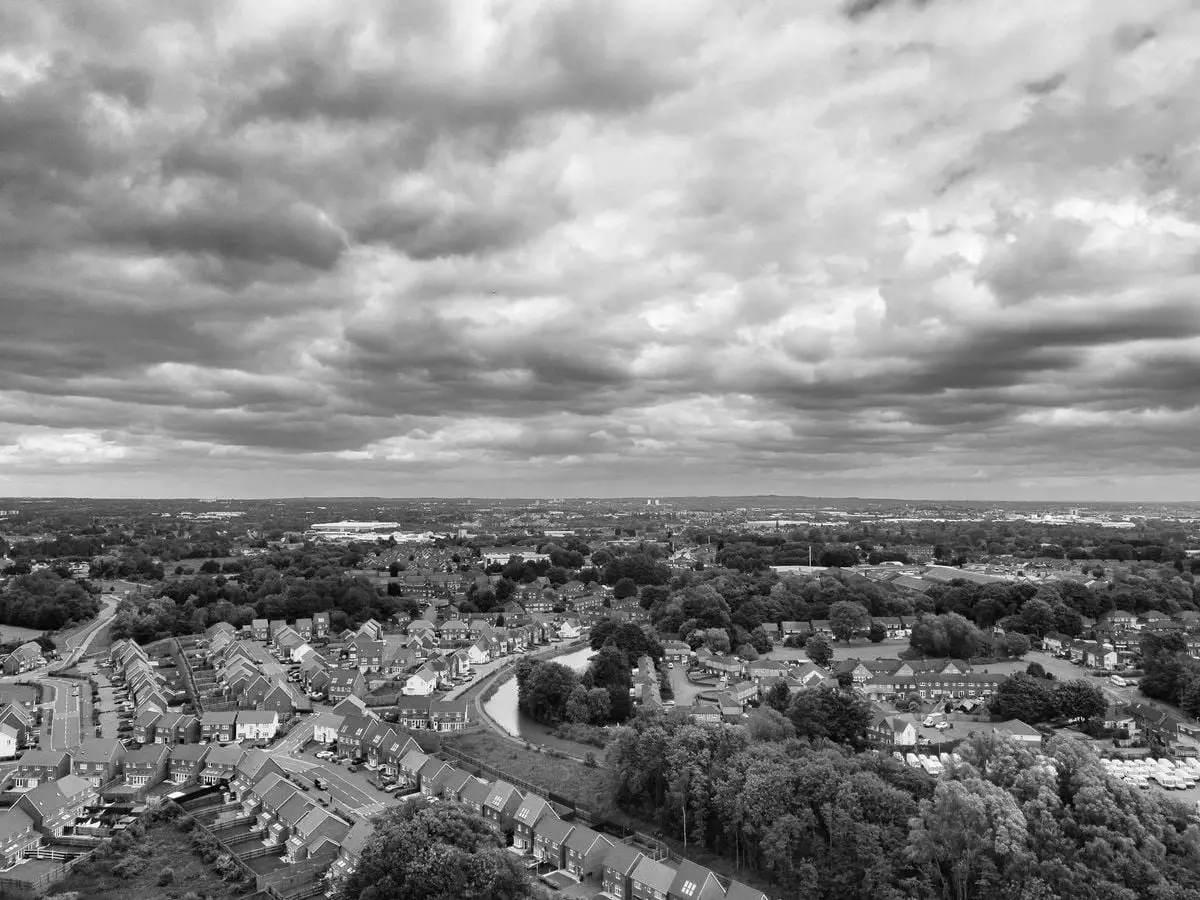 Black and white aerial photo of a suburban neighborhood under dramatic clouds.