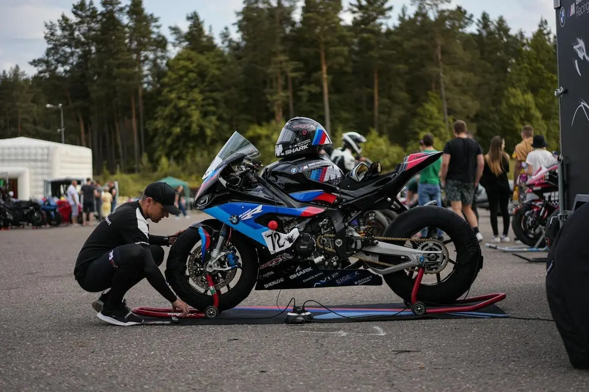 Man preparing sports motorcycle for race, with team support outdoors.