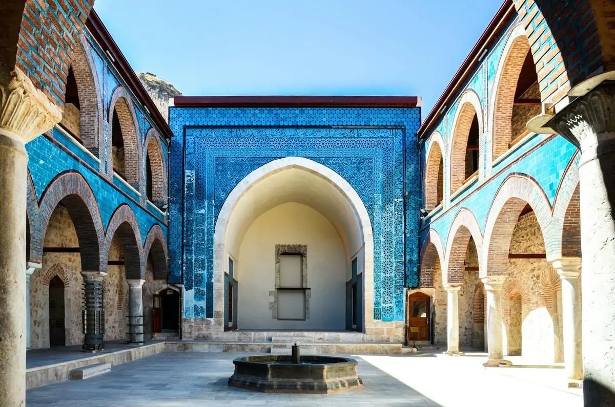 A vibrant courtyard with classic Seljuk architecture features intricate turquoise tiles and arches.