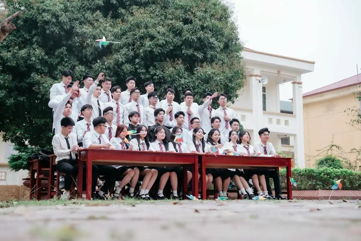 A group of high school students in uniforms celebrating outside on a sunny day.