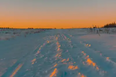 A scenic winter landscape of snow-covered fields under a vibrant sunset sky.