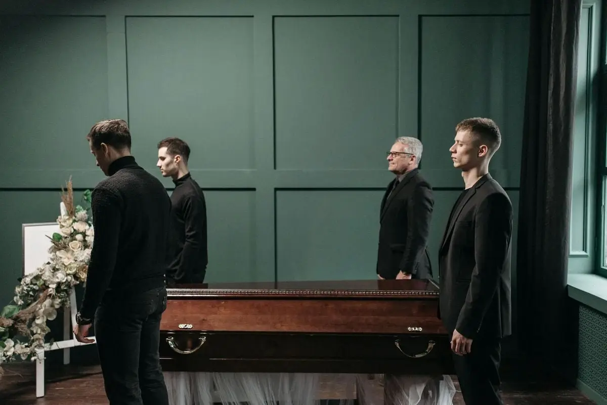 Four men in black suits standing at a funeral, symbolizing loss and mourning indoors.