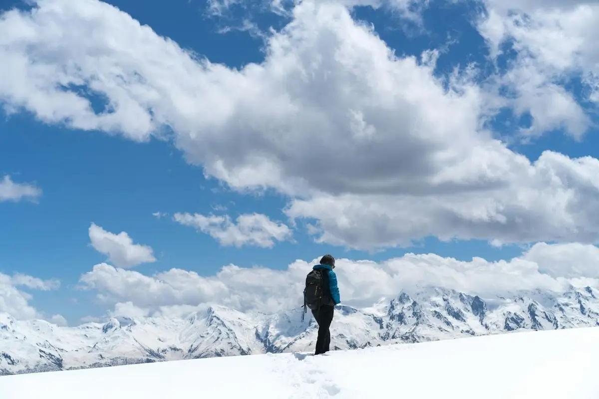 A lone hiker with backpack exploring snow-covered mountains under a bright sky.