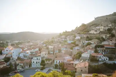 A serene aerial view of a Greek old town with houses on a hillside during sunset, offering a picturesque landscape.