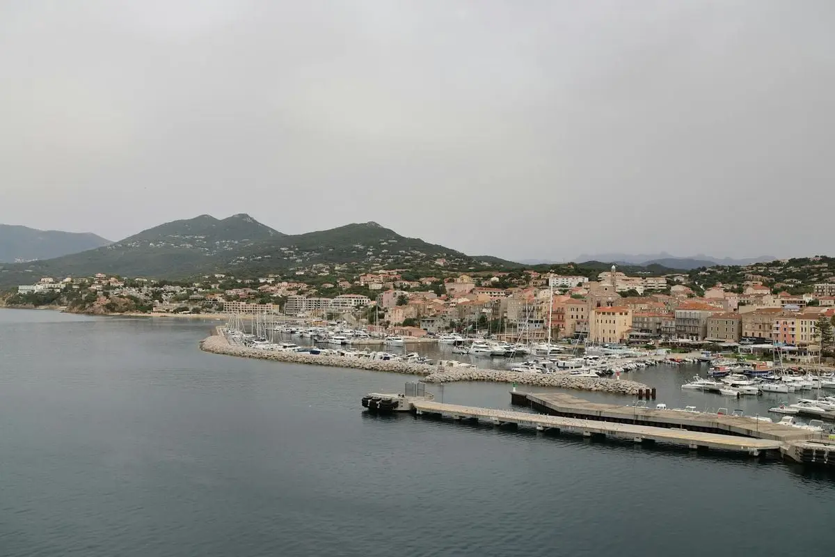 Picturesque harbor view of a Mediterranean coastal town with moored boats and stunning hillside backdrop.