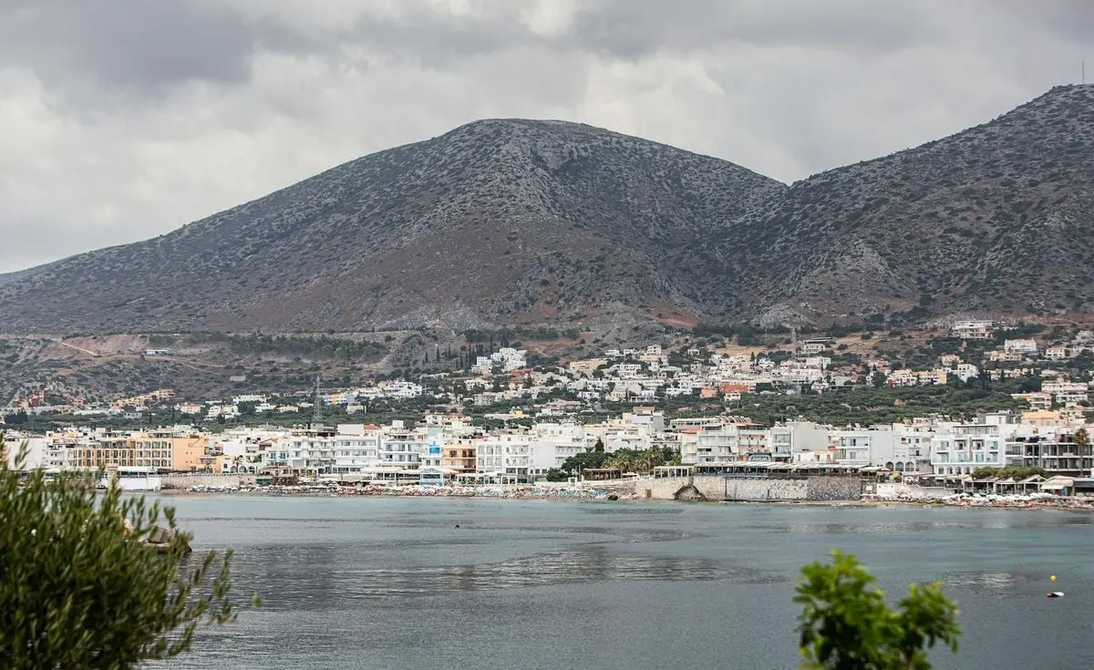 Charming coastal town with hills and sea under a cloudy sky.