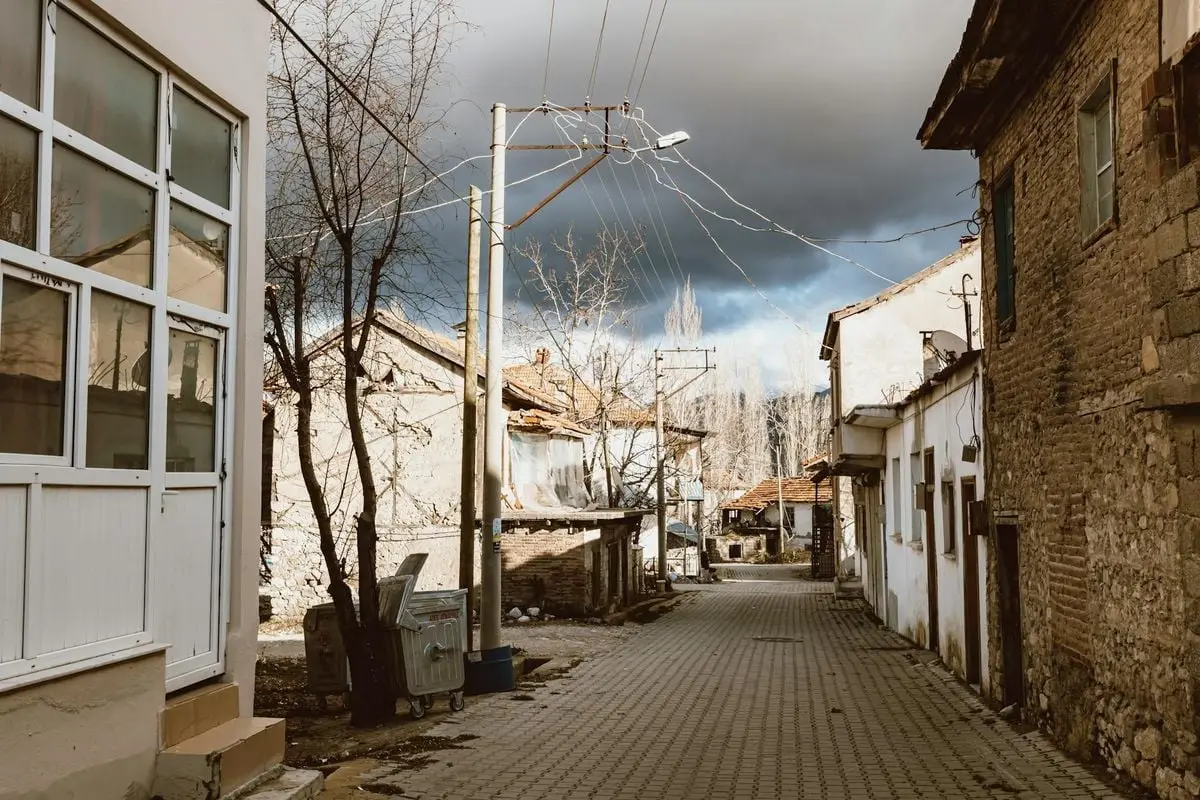 A narrow alleyway lined with rustic buildings under a dramatic sky in a quaint town.