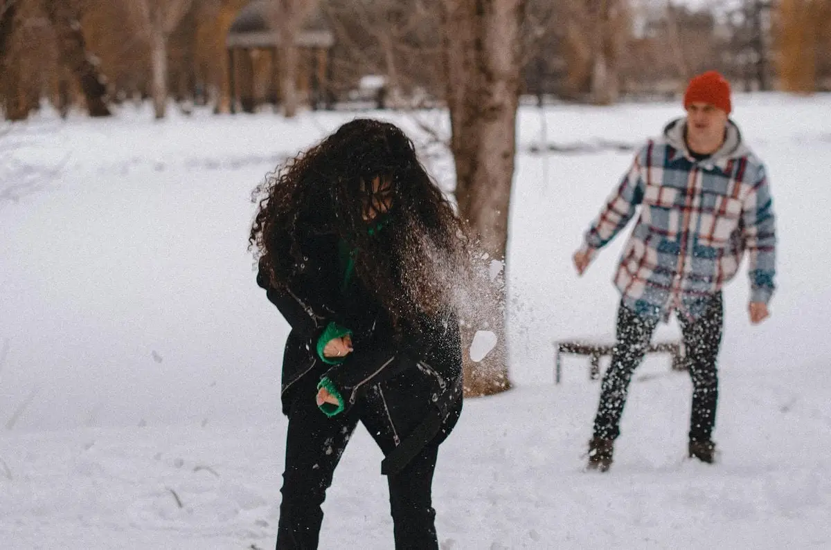 Couple having fun throwing snowballs in winter park, enjoying the cold weather.