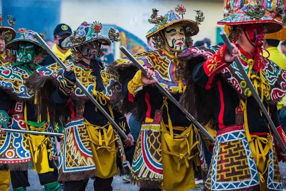 Masked performers in colorful traditional costumes parade during a vibrant cultural festival in Taiwan.
