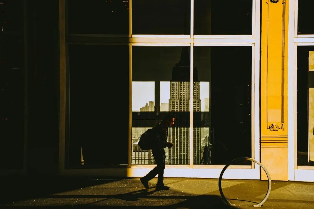 Silhouette of a person walking in front of window reflection showing a city skyline at golden hour.