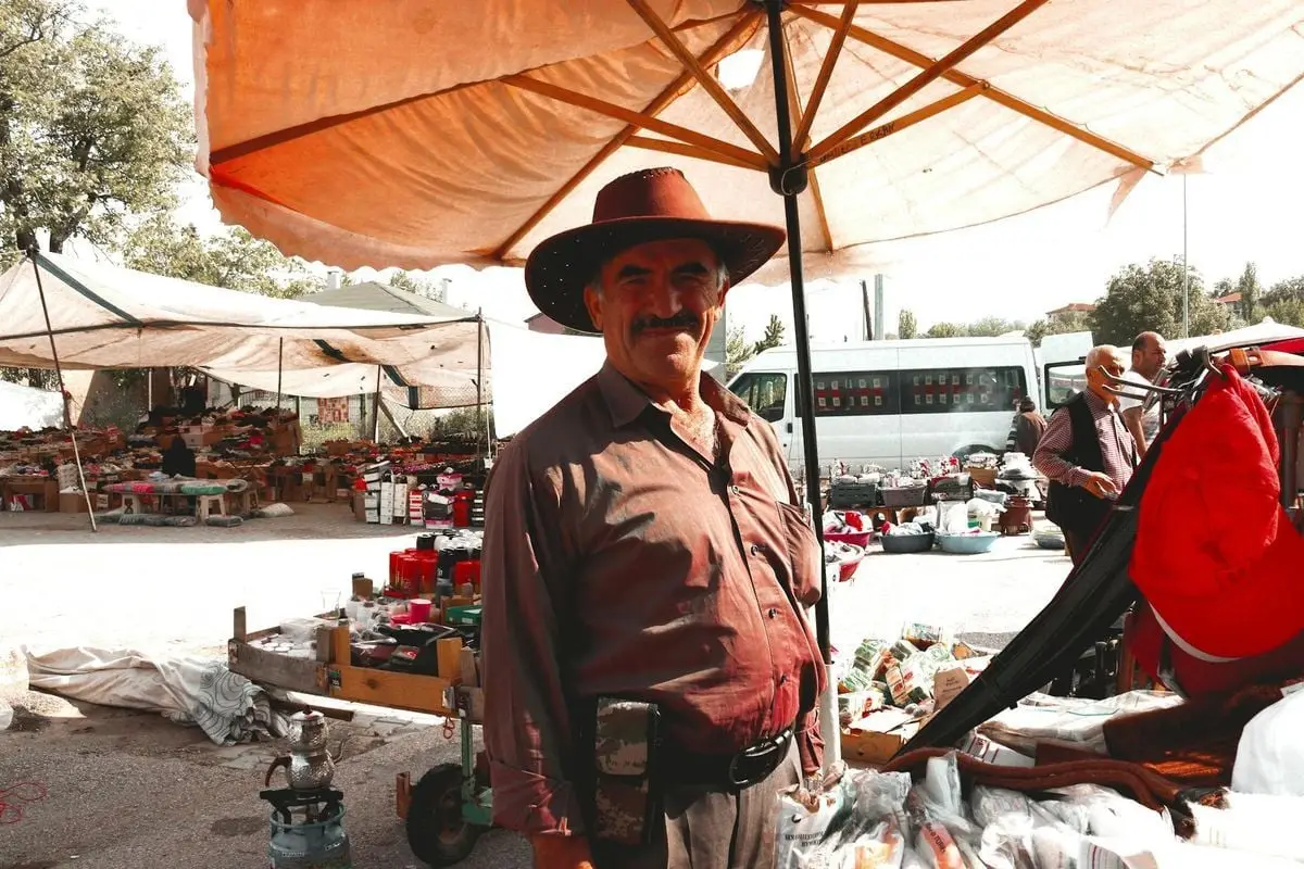 Smiling vendor wearing a hat at Hamamözü market in Türkiye, showcasing traditional bazaar life.