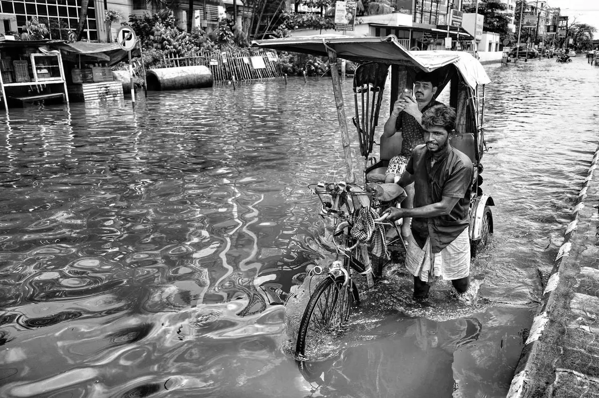 A rickshaw puller navigates through a flooded street in Kolkata, India, capturing resilience.
