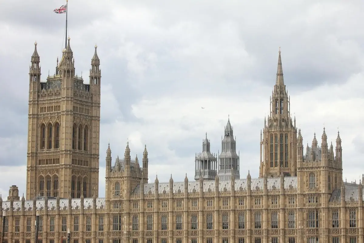 Detailed view of the Gothic architecture of the Palace of Westminster, London under a cloudy sky.