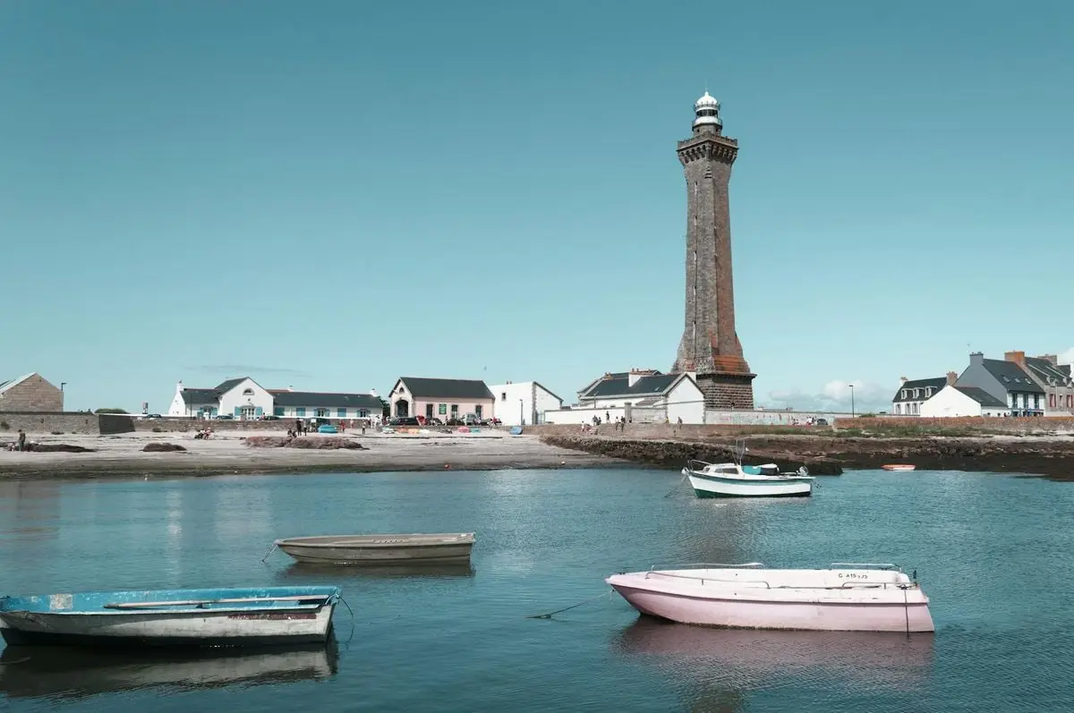 A scenic view of the Penmarc'h Lighthouse with boats docked in a serene harbor in Brittany, France.