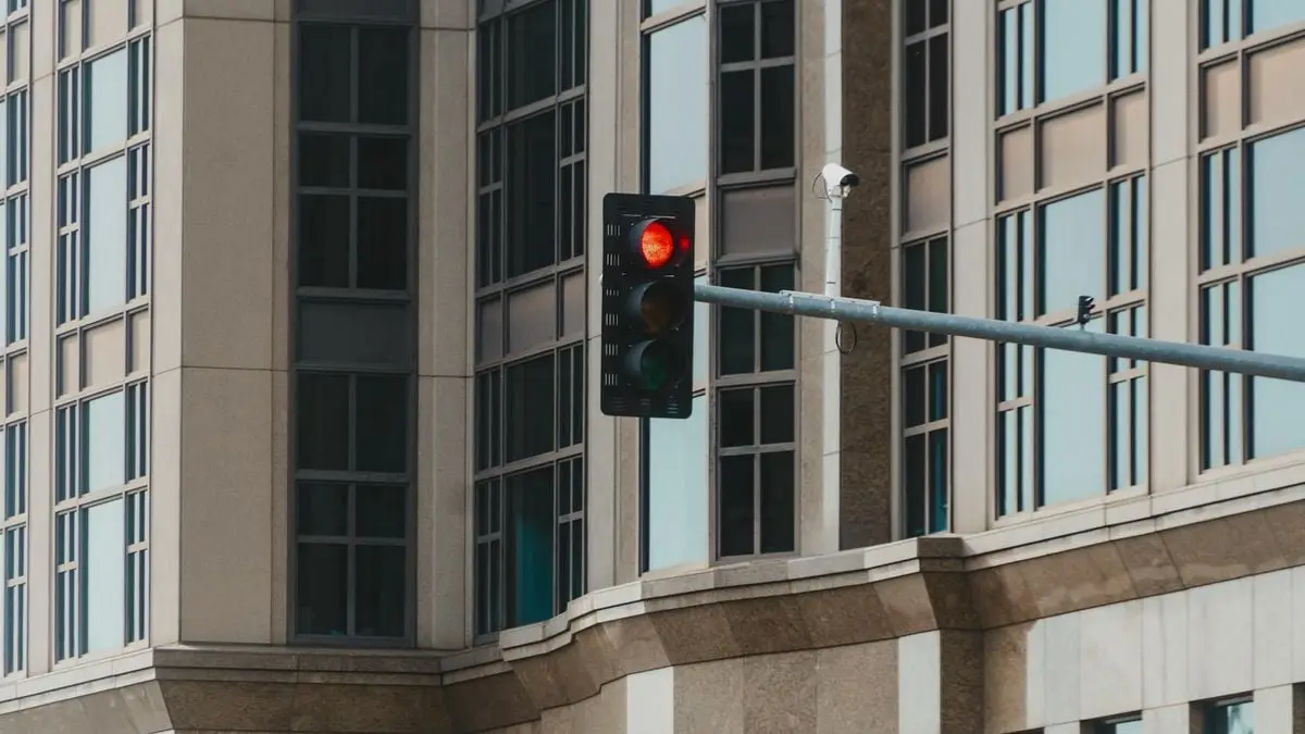 Red traffic light in cityscape setting with modern glass building facade.