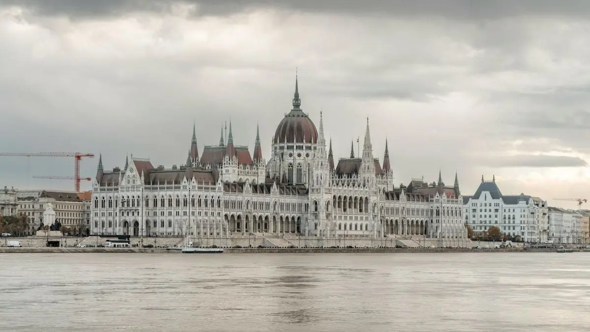Majestic view of Budapest's Parliament building along the Danube River under dramatic skies.