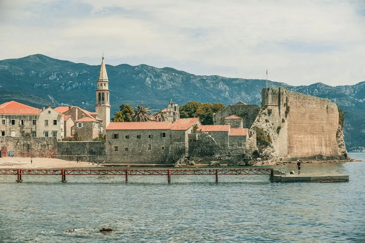 Aged temple facades and tower near rippled sea with pier behind ridge under cloudy sky