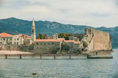 Aged temple facades and tower near rippled sea with pier behind ridge under cloudy sky